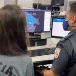 Dois agentes da Polícia Civil em frente a um computador olhando um mapa da zona central da cidade do Rio de Janeiro.