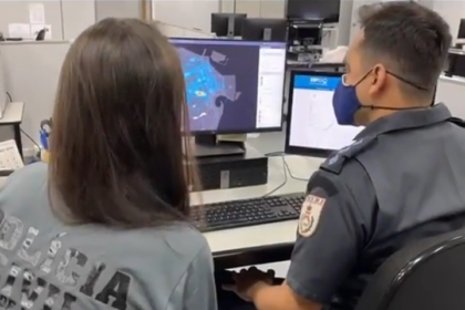 Dois agentes da Polícia Civil em frente a um computador olhando um mapa da zona central da cidade do Rio de Janeiro.