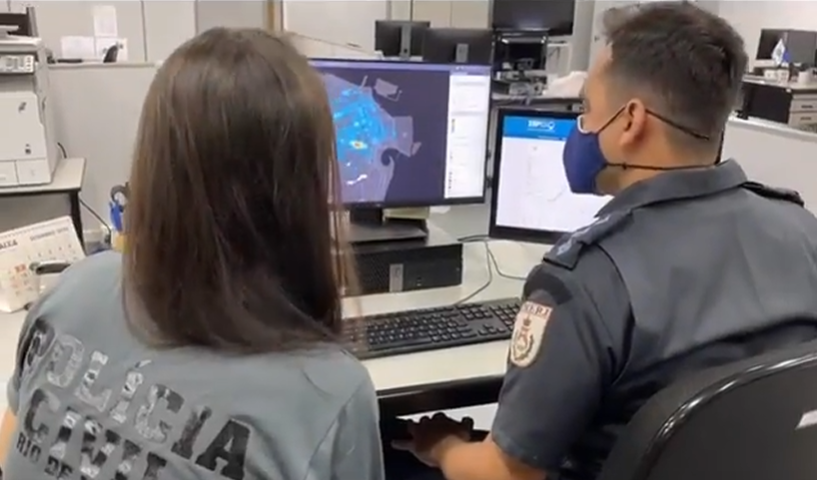 Dois agentes da Polícia Civil em frente a um computador olhando um mapa da zona central da cidade do Rio de Janeiro.