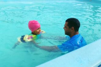 Vila Olímpica Didi abre 547 vagas gratuitas para prática esportiva. Imagem de criança na piscina com instrutor.