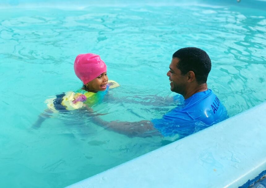 Vila Olímpica Didi abre 547 vagas gratuitas para prática esportiva. Imagem de criança na piscina com instrutor.