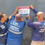 Agentes da Seop colam adesivo em portão