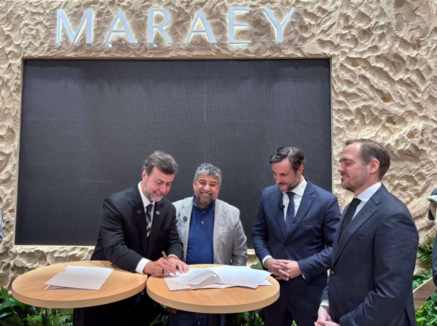 Marcelo Freixo, presidente da Embratur, assina documento durante a FITUR, em Madri, ao lado do prefeito de Maricá, Washington Quaquá, e representantes do setor turístico.