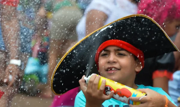 Criança brinca com espuma durante bloco infantil no Rio; programação do carnaval 2026 inclui desfiles mirins na Sapucaí e opções para famílias em diferentes regiões da cidade.