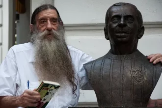 Foto de Nelsinho ao lado de um busto do pai, Nelson Rodrigues