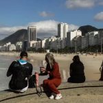 Sol e casaco: cariocas e turistas aproveitam o sábado de tempo estável na mureta da Praia do Leme, na Zona Sul do Rio. Fim de semana terá céu aberto, máxima de 28°C e madrugadas frias, com mínima de 13°C na capital.