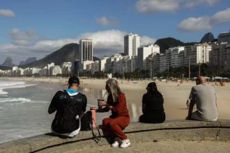 Sol e casaco: cariocas e turistas aproveitam o sábado de tempo estável na mureta da Praia do Leme, na Zona Sul do Rio. Fim de semana terá céu aberto, máxima de 28°C e madrugadas frias, com mínima de 13°C na capital.