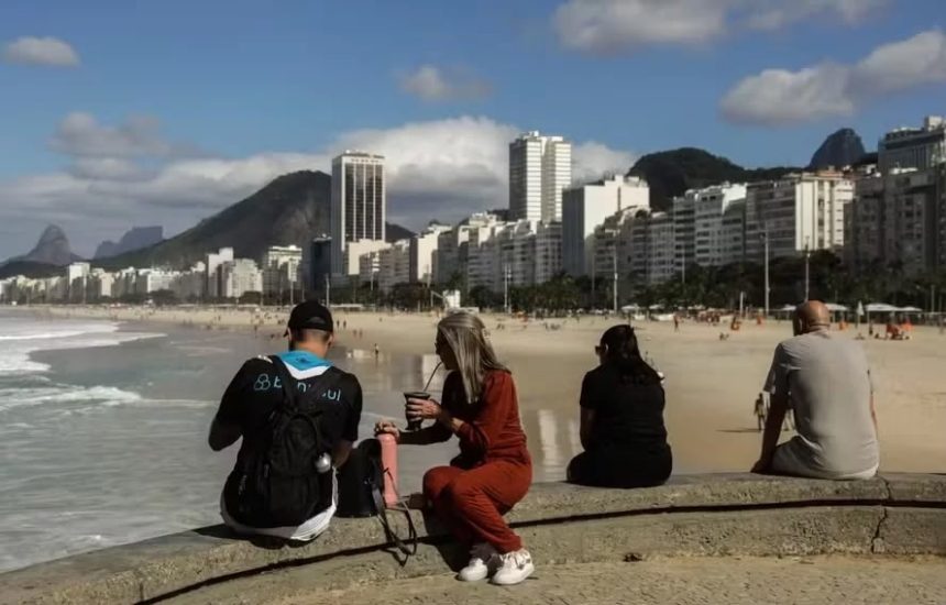 Sol e casaco: cariocas e turistas aproveitam o sábado de tempo estável na mureta da Praia do Leme, na Zona Sul do Rio. Fim de semana terá céu aberto, máxima de 28°C e madrugadas frias, com mínima de 13°C na capital.