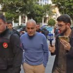 Davi Perini Vermelho, o Didê, (no meio, de camisa azul), chega à delegacia no dia da prisão