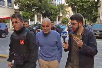 Davi Perini Vermelho, o Didê, (no meio, de camisa azul), chega à delegacia no dia da prisão
