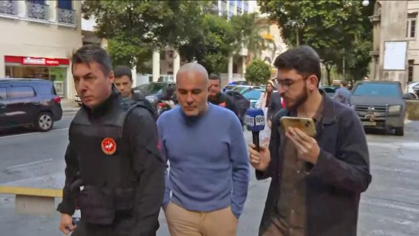 Davi Perini Vermelho, o Didê, (no meio, de camisa azul), chega à delegacia no dia da prisão